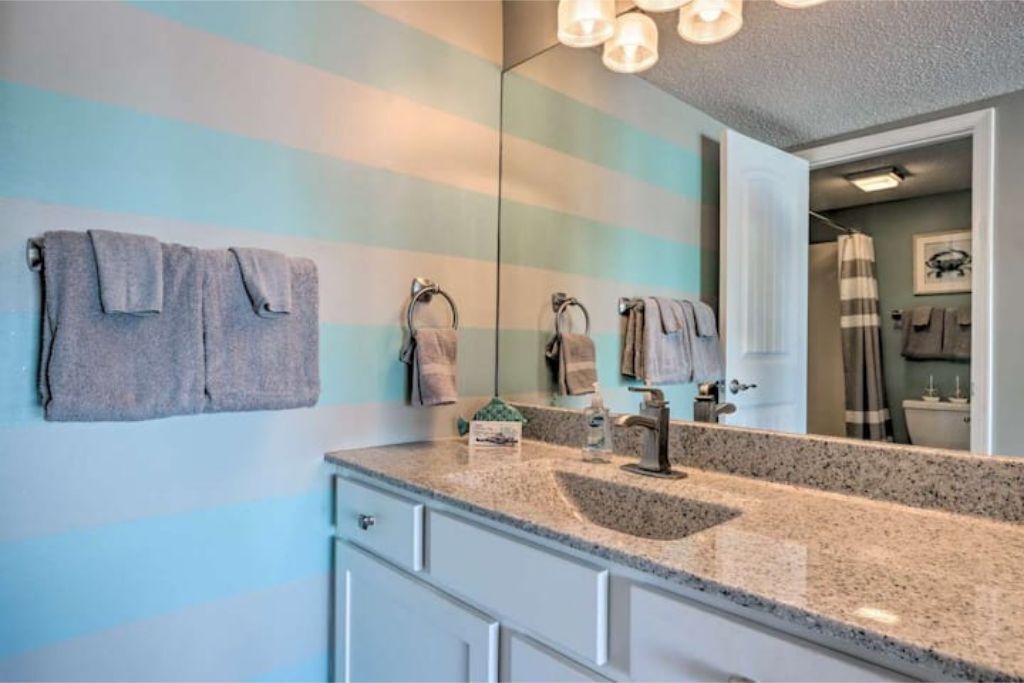 A bathroom with striped walls, a granite sink, and a mirror.