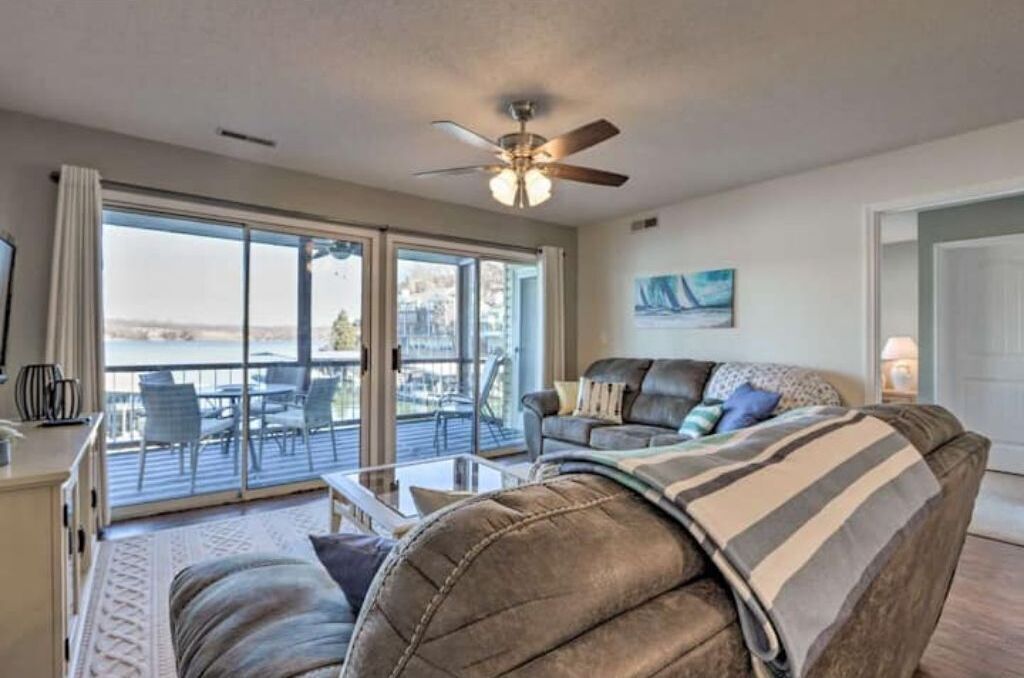 A living room with a sofa, a coffee table, and a ceiling fan. There is a sliding glass door leading to an outdoor area with chairs and a table.