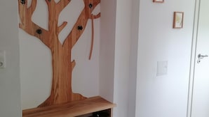 Una habitación con una estantería con forma de árbol de madera, ganchos, una puerta blanca y un pequeño cuadro en la pared.