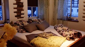 Un dormitorio con cama de madera, ropa de cama floral, una lámpara colgante y un adorno de pared de piedra.