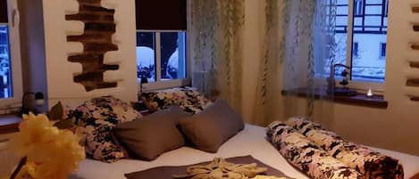 A bedroom with a wooden bed, floral bedding, a hanging light fixture, and a stone wall decoration.