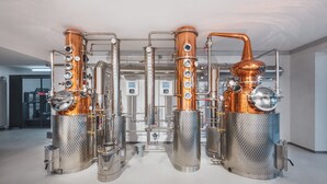 Una destilería con equipos de cobre y acero inoxidable, incluyendo columnas y tanques grandes, ubicada en un amplio espacio industrial.