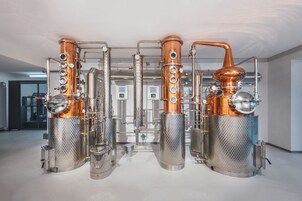 Una destilería con equipos de cobre y acero inoxidable, incluyendo columnas y tanques grandes, ubicada en un amplio espacio industrial.
