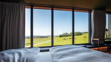 Ein Schlafzimmer mit großem Fenster mit Blick auf ein grünes Feld mit Kühen.