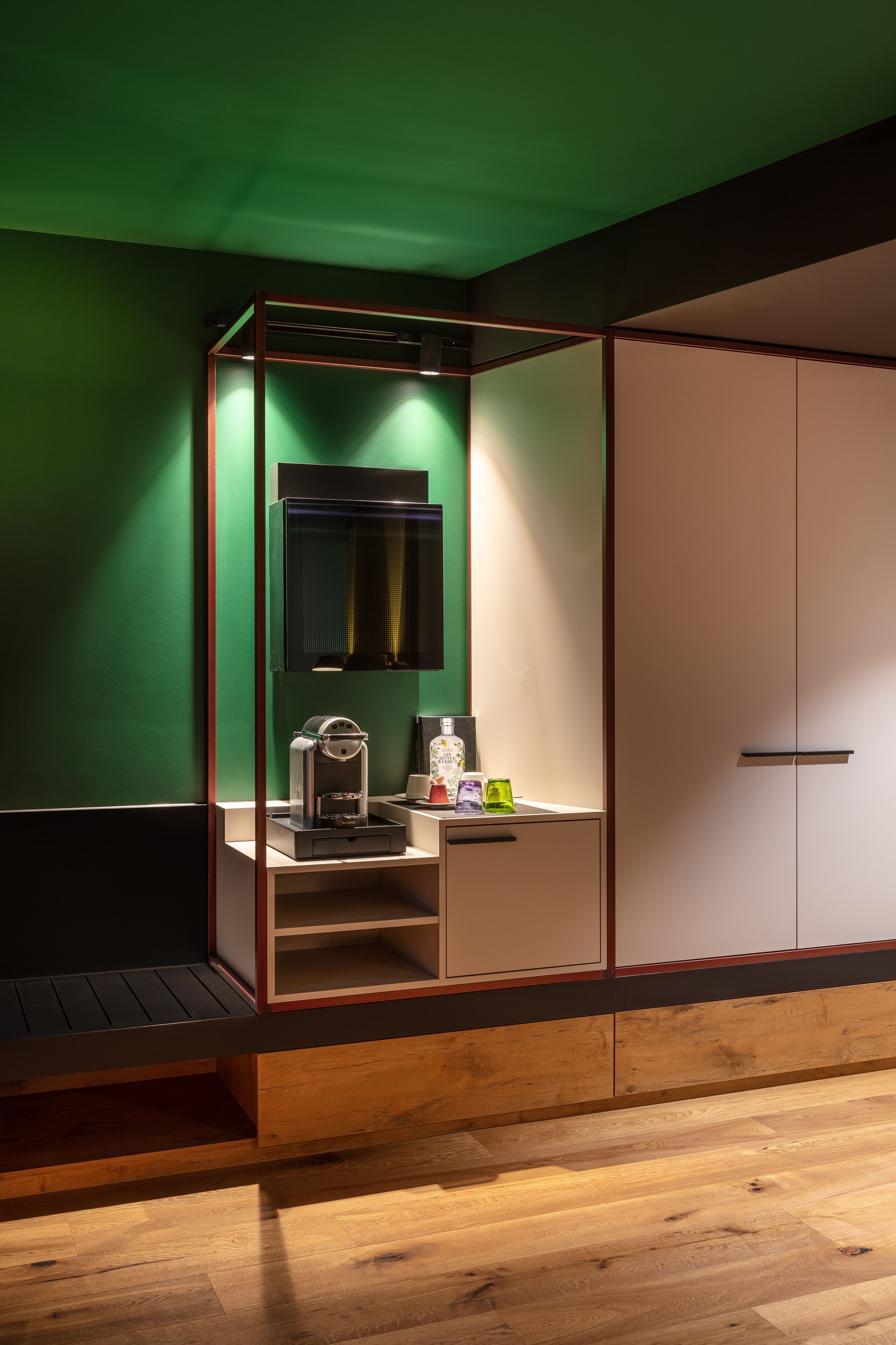 A room with a green wall, a wooden bench, a coffee machine, and a cabinet with a mirror.