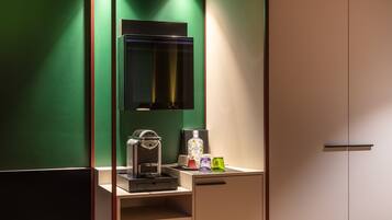 A room with a green wall, a wooden bench, a coffee machine, and a cabinet with a mirror.