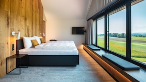 Un dormitorio moderno con una cama grande, paneles de madera, un televisor y vistas a un paisaje verde.