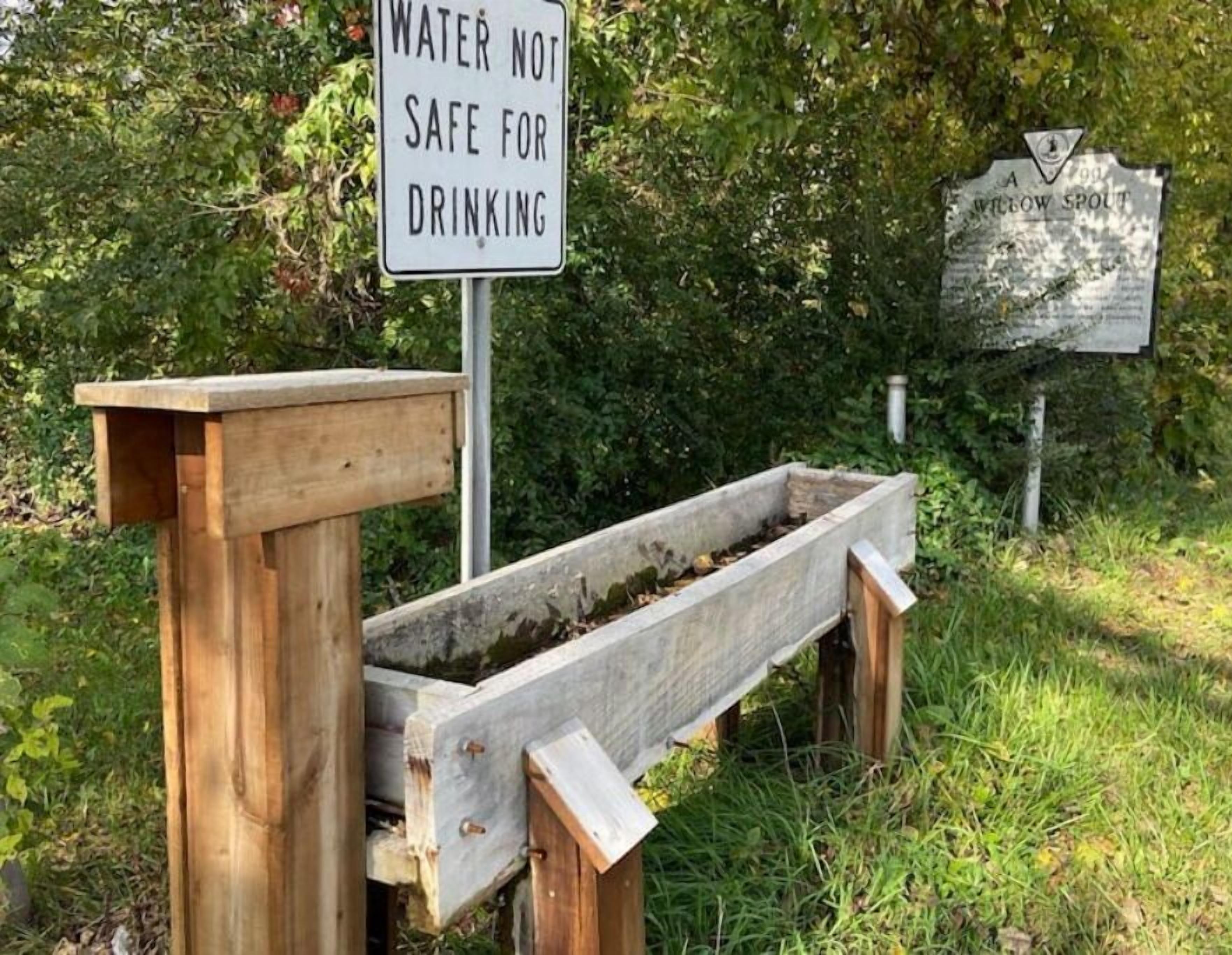 A wooden water filtration system with a sign stating "WATER NOT SAFE FOR DRINKING" and a signboard labeled "A WILLOW SPOT".