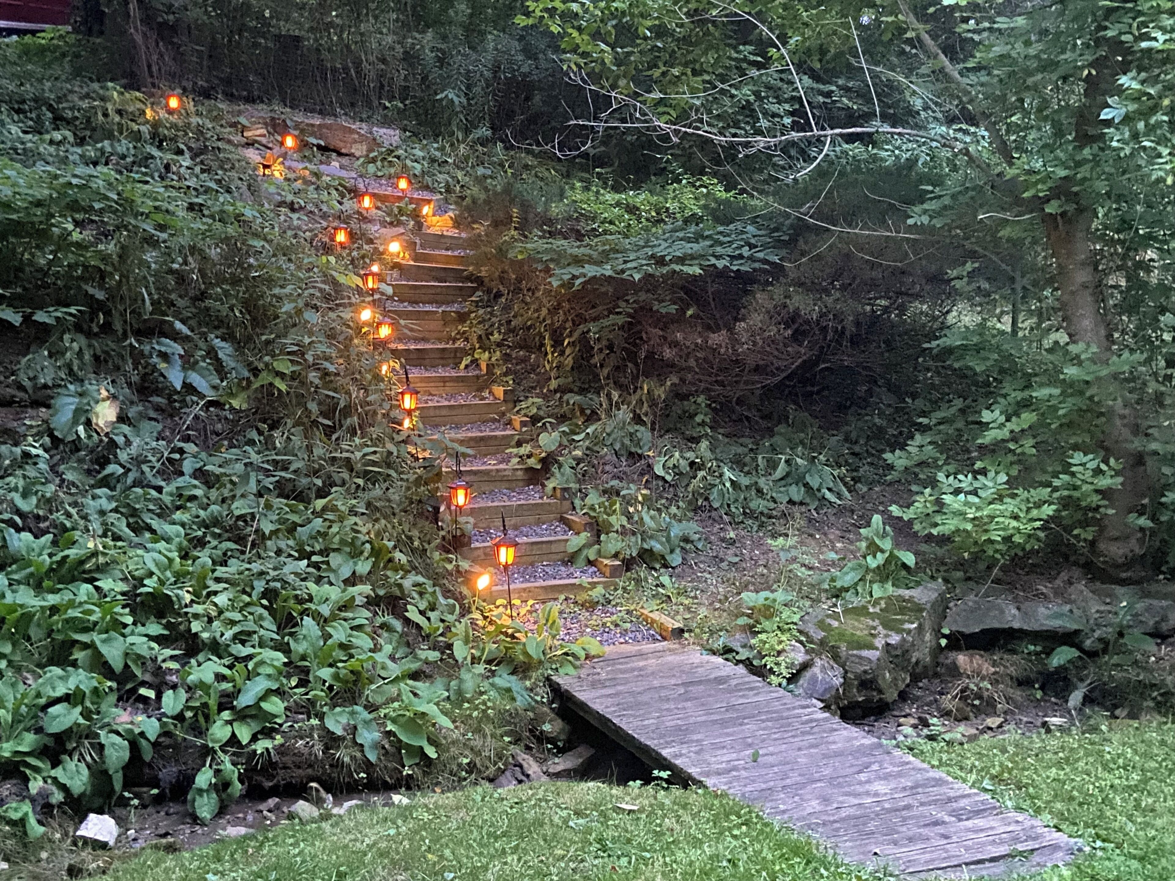 A wooden staircase with lanterns, surrounded by greenery.