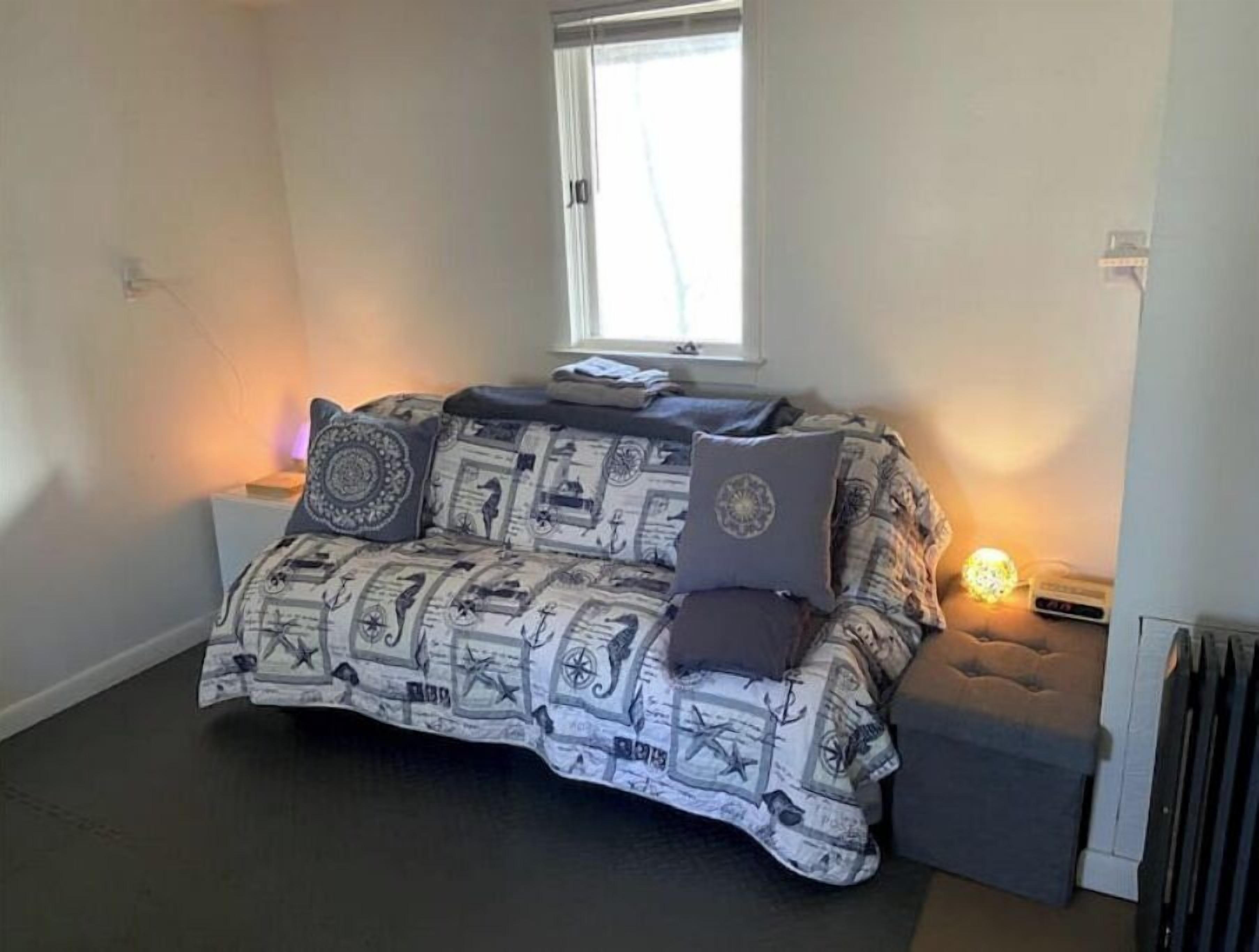A small, cozy room with a patterned sofa, a window, and a bedside lamp.