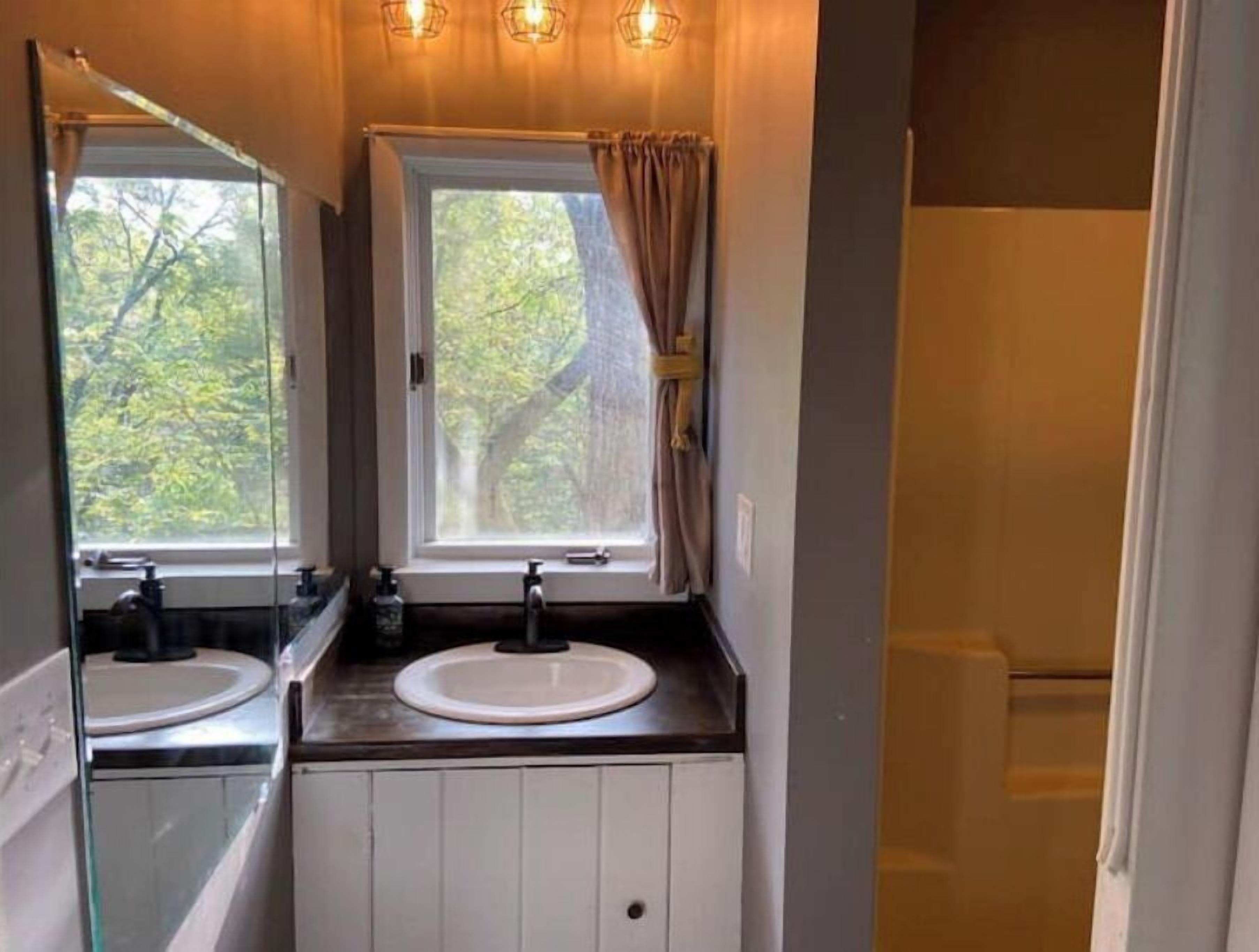 A bathroom with a double sink, a window with curtains, and a mirror.