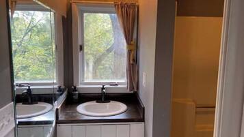 A bathroom with a double sink, a window with curtains, and a mirror.