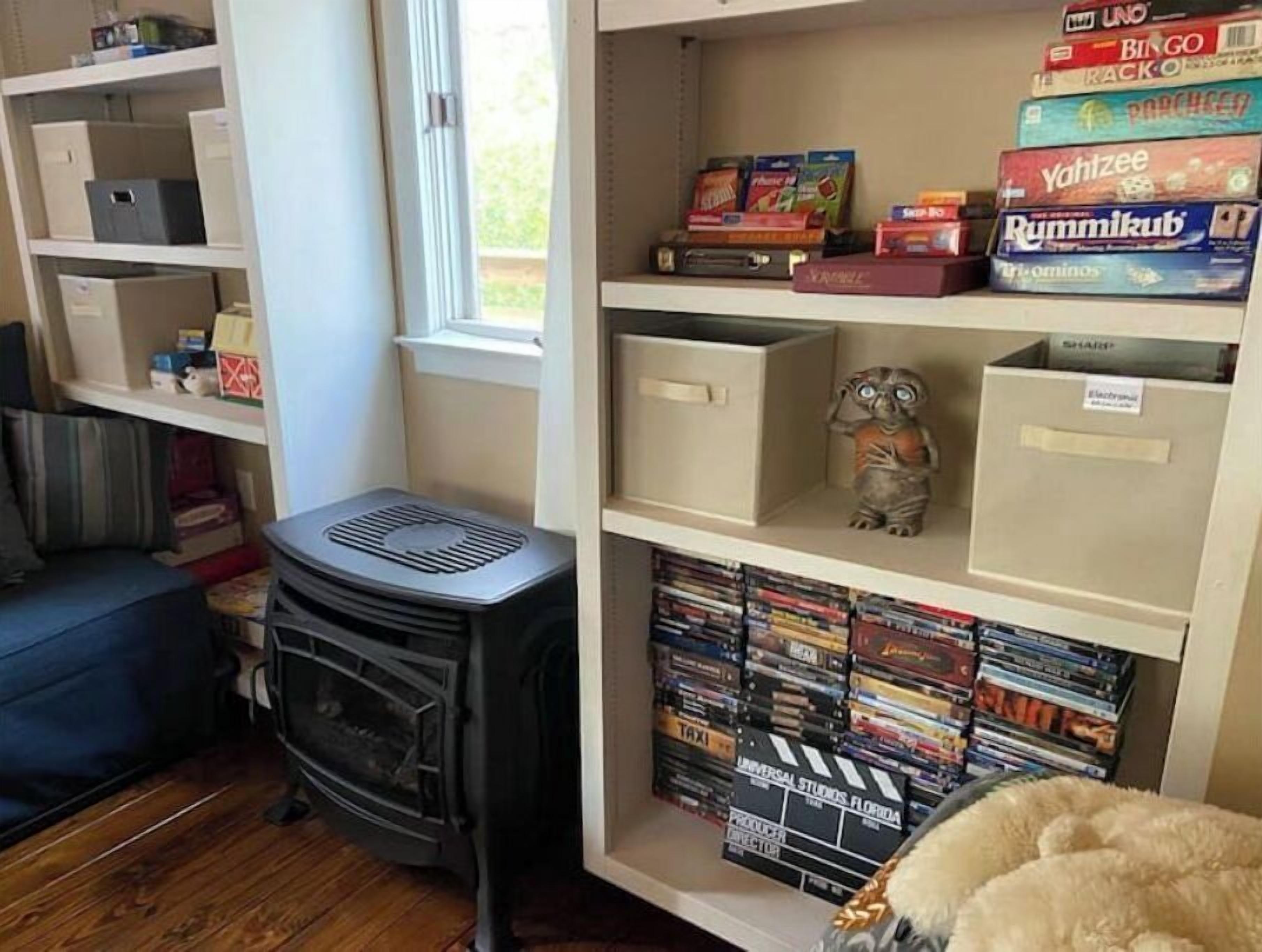A room with a fireplace, a bookshelf with board games, and a window.