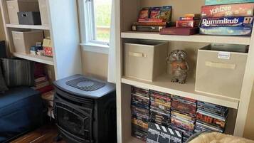A room with a fireplace, a bookshelf with board games, and a window.