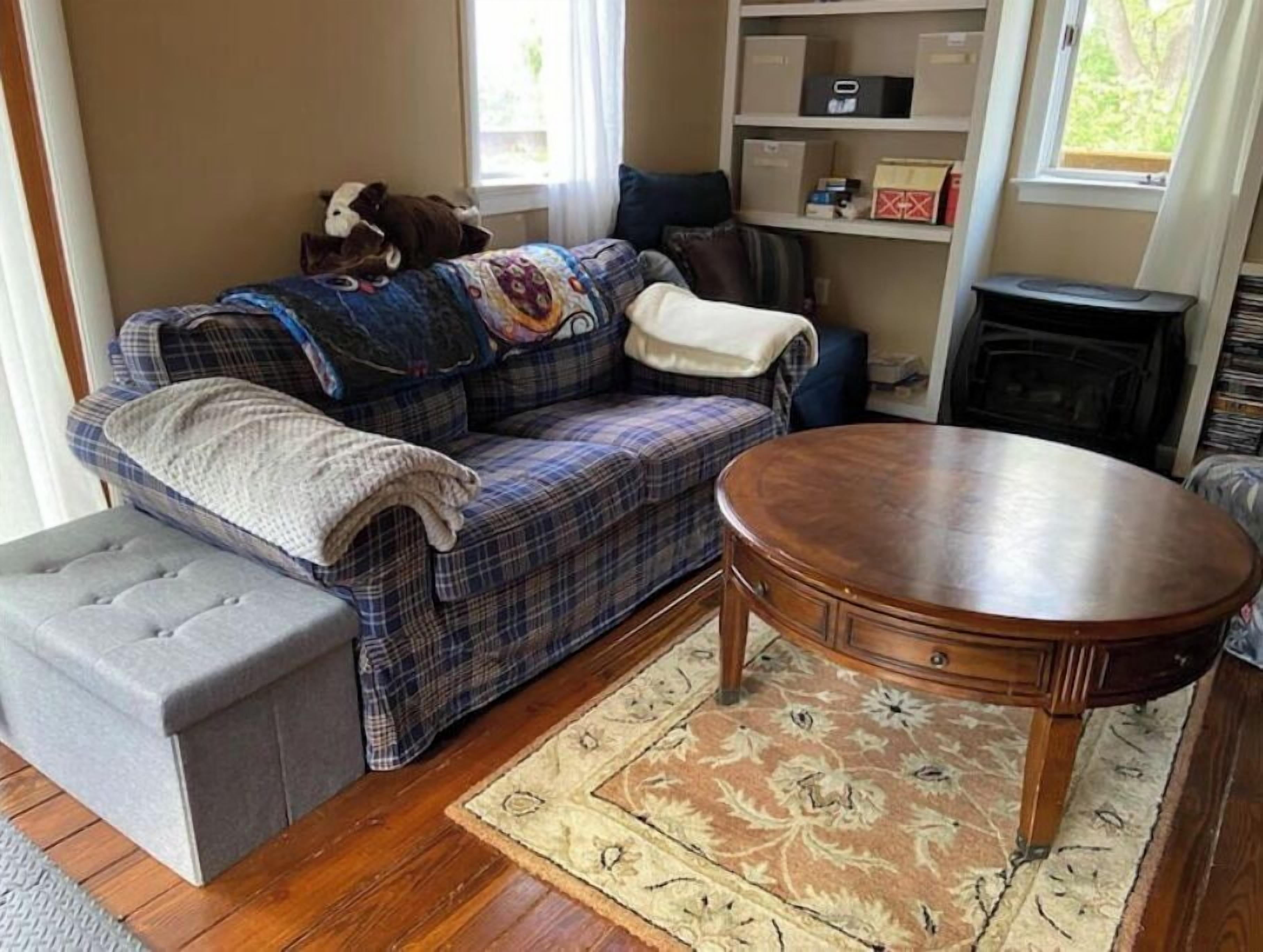 Un salon chaleureux avec un canapé à carreaux, un pouf gris, une table basse en bois et un tapis à motifs.