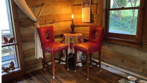 L’intérieur d’un chalet accueillant, avec des murs en bois, deux fauteuils en cuir rouge, une petite table ronde et une fenêtre donnant sur un paysage verdoyant.