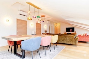 Ein modernes Wohnzimmer mit einem Holzesstisch, bunten Stühlen, einem Sofa und einem Fernseher.