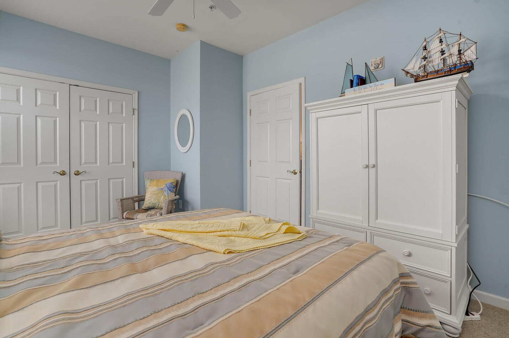 Een slaapkamer met een bed, twee kasten, een stoel en een plafondventilator.