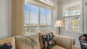 A room with a large window, a sofa with floral cushions, and a lamp.