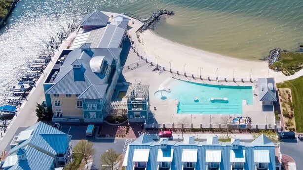 An aerial view of a coastal hotel with a large swimming pool, beach access, and multiple buildings with blue roofs.