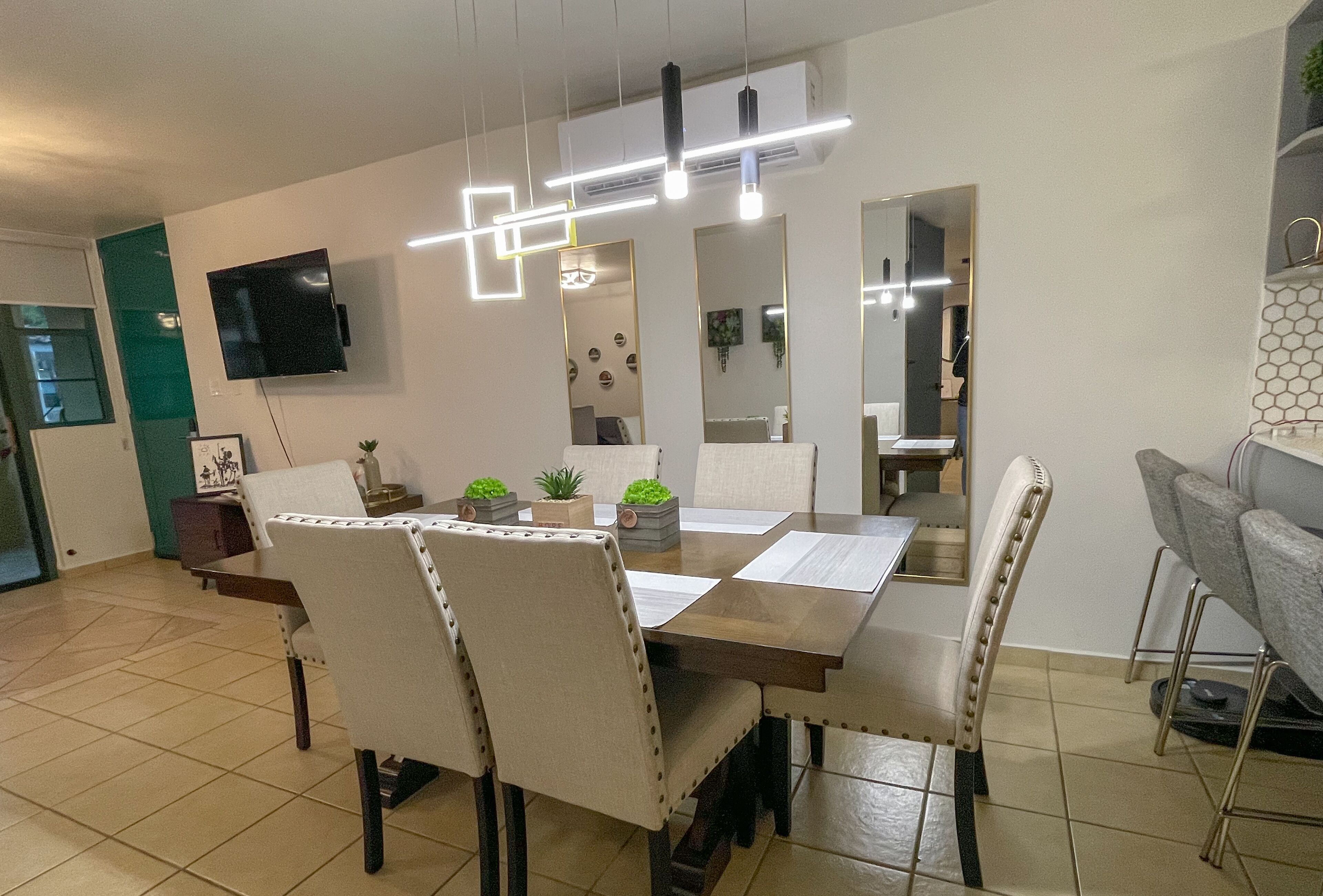 A dining area with a rectangular table, four chairs, and a flat-screen TV mounted on the wall.