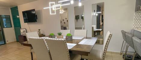 A dining area with a rectangular table, four chairs, and a flat-screen TV mounted on the wall.
