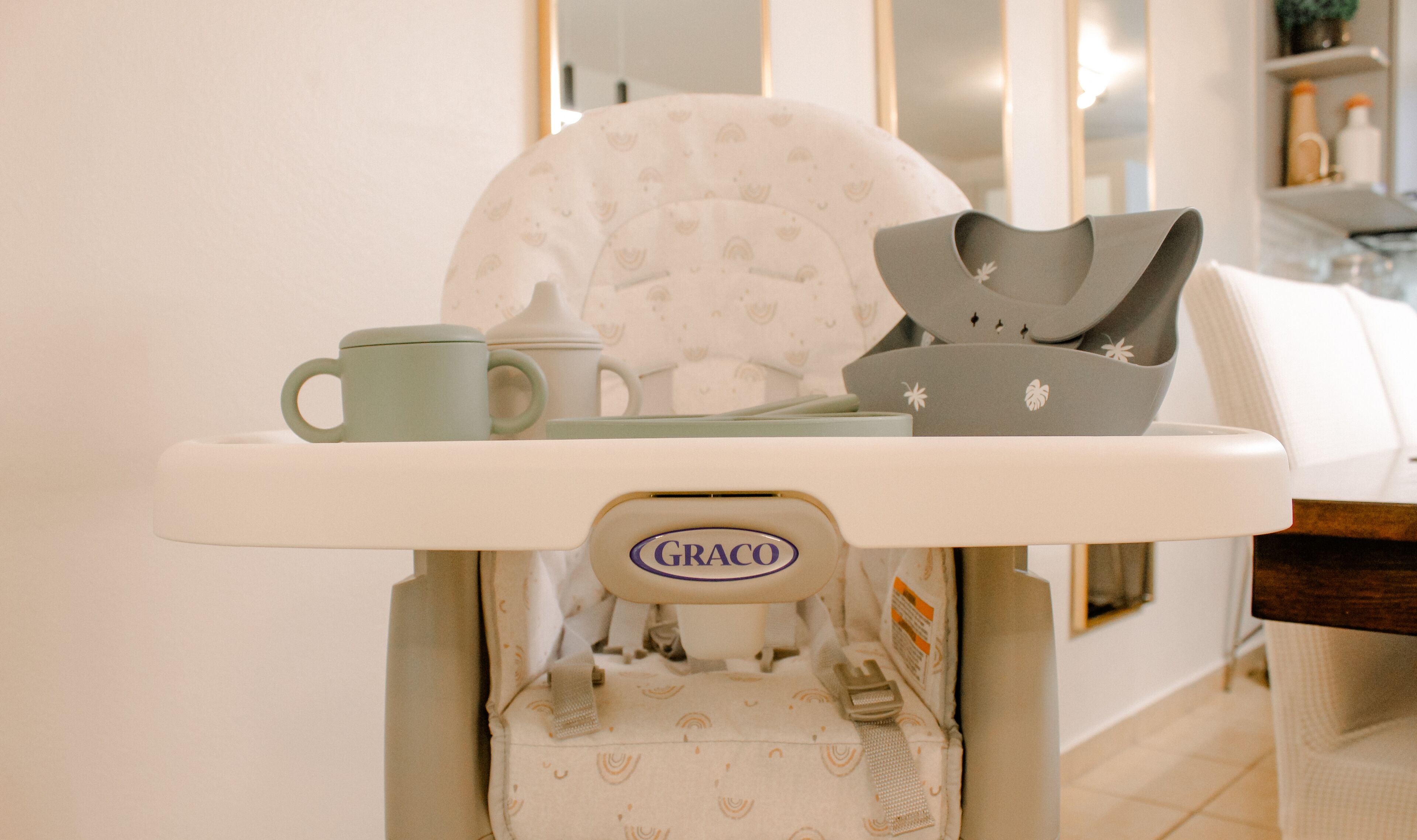 Une chaise haute de la marque Graco, avec un gobelet et un bol.