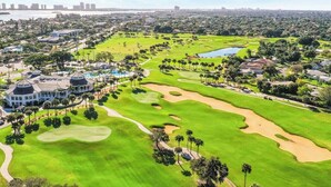 A golf course with a clubhouse, palm trees, and a view of a city skyline. - 3 Bed, 2 Bath - North Palm Beach! (North Palm Beach)