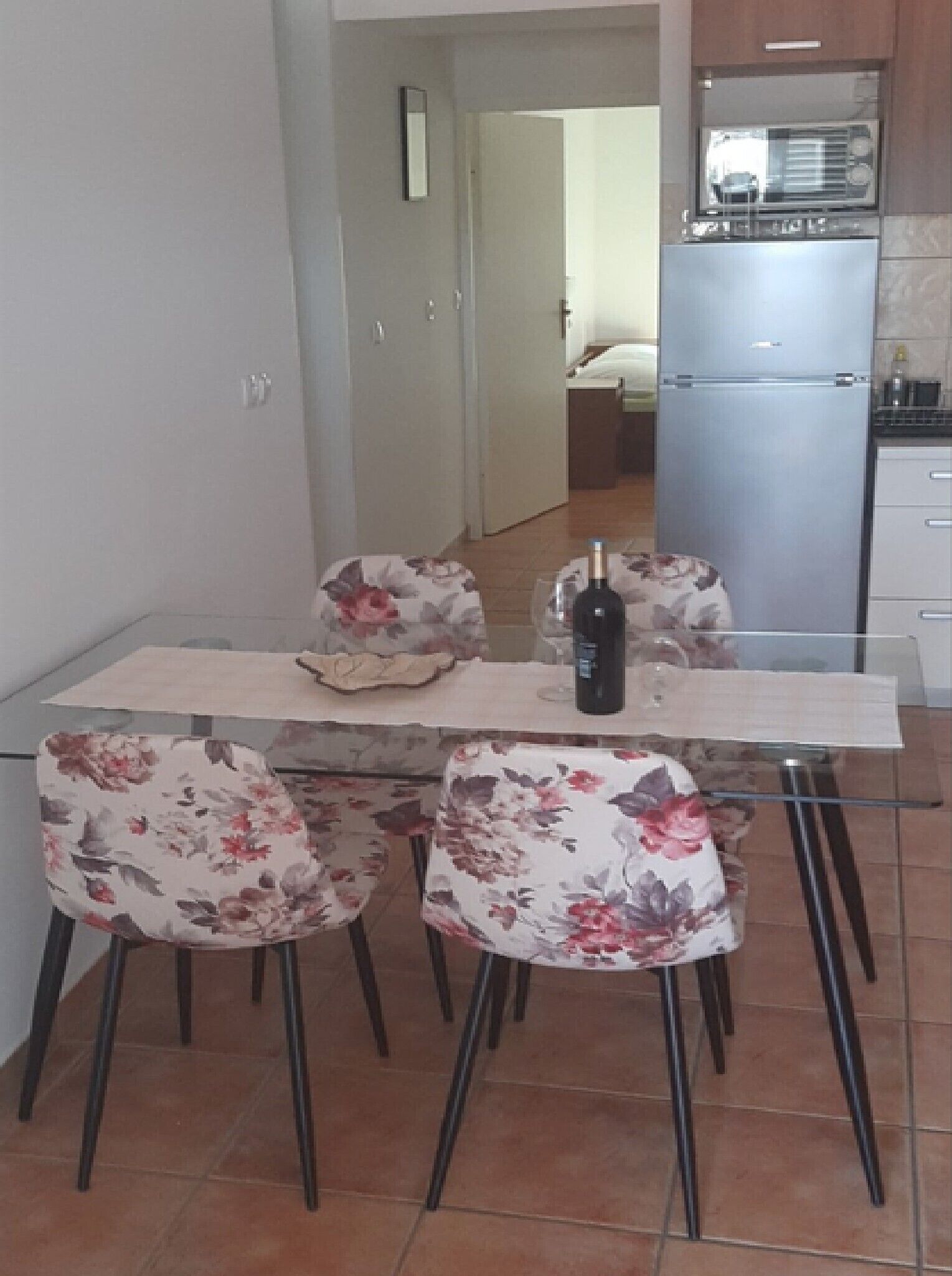 A dining area with a table set for two, two chairs with floral upholstery, a bottle of wine, and a glass.
