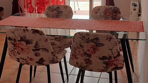 Zona pranzo con tavolo in vetro e sedie floreali, TV a parete e vista su un balcone con un panorama suggestivo.