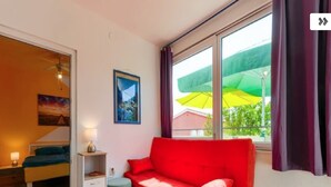 Una habitación con una cama, un sofá rojo, una mesita y una ventana con cortinas.