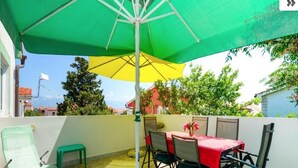 Un patio con un paraguas verde y amarillo, una mesa con sillas y una silla verde.