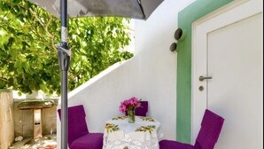 Ein kleiner Patio-Bereich mit Tisch und zwei Stühlen, einer Tür und einer grünen Wand.