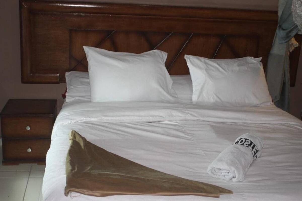 A bed with white linens, a wooden headboard, and a brown throw blanket.