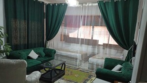 Ein Wohnzimmer mit zwei grünen Sofas, einem weißen Sessel, einem Glastisch und einem gemusterten Teppich.