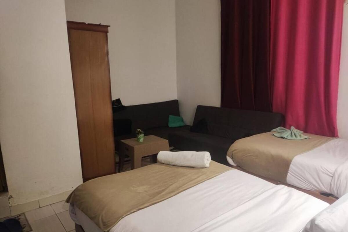 A hotel room with two beds, a desk, a chair, a wardrobe, and a red curtain.