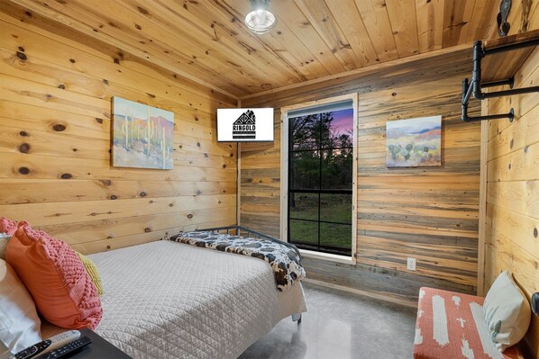 Quarto de cabana de madeira com cama, quadros, janela e uma placa na parede.
