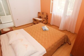 Quarto com cama, uma mesinha, uma cadeira e janela com cortinas.