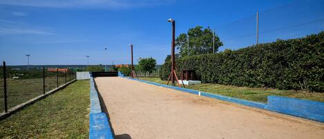 A clear, sunny day at a sports facility with a dirt track, blue safety barriers, and a chain-link fence.
