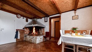 Un interior rústico con chimenea de piedra, vigas de madera, una mesa de comedor para dos personas y un reloj en la pared.