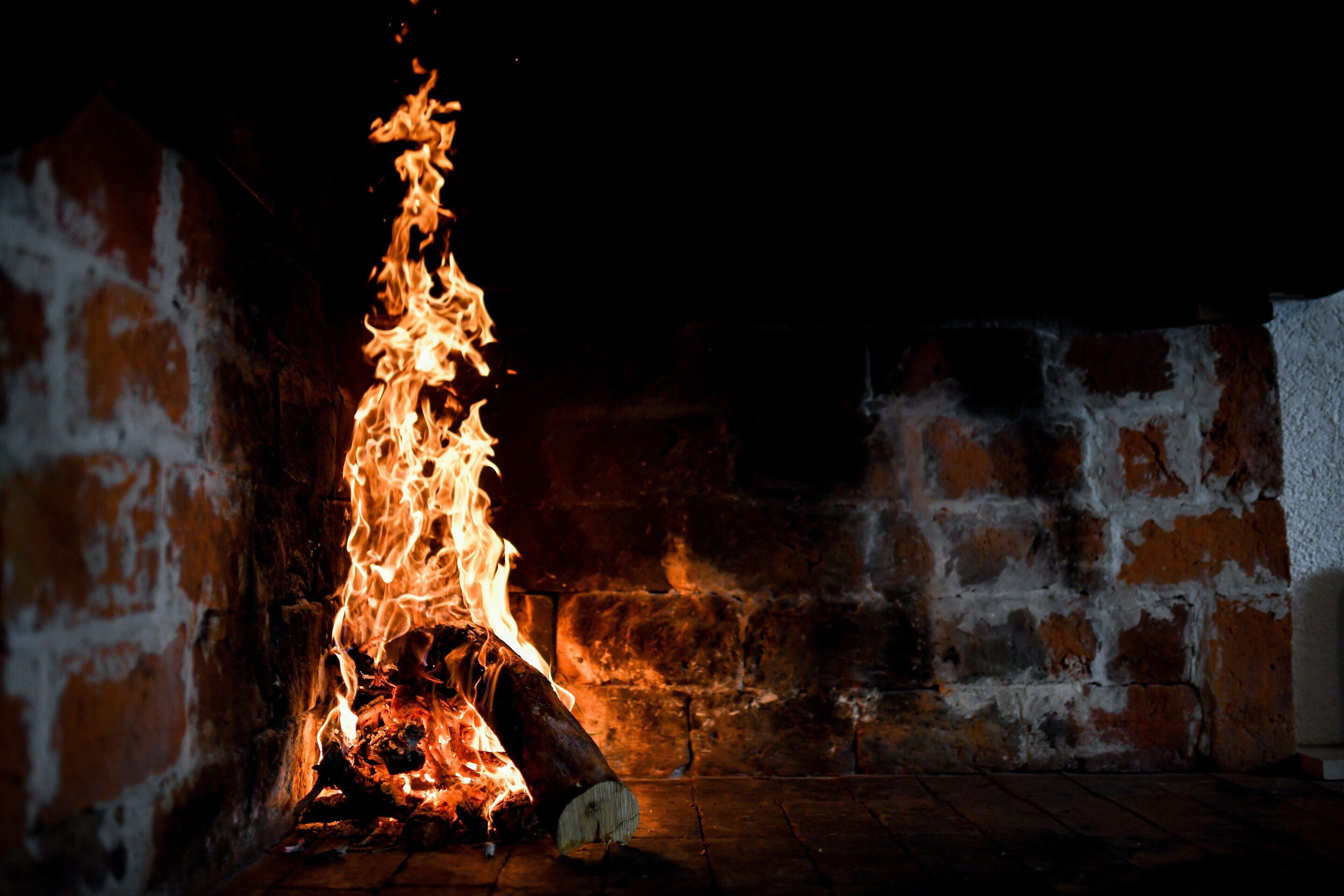 Una chimenea con leña ardiendo y llamas, ubicada en una habitación con paredes de ladrillo.