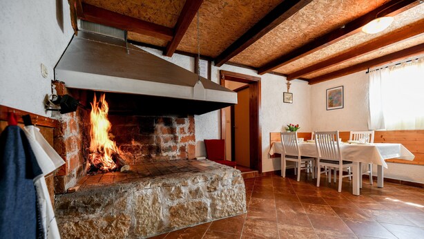 Una chimenea de piedra con fuego a la vista, una mesa de comedor con sillas y un techo de madera.