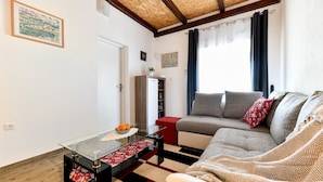 Una sala de estar con una mesa de centro de vidrio, un sofá, un reposapiés rojo y techo de madera.