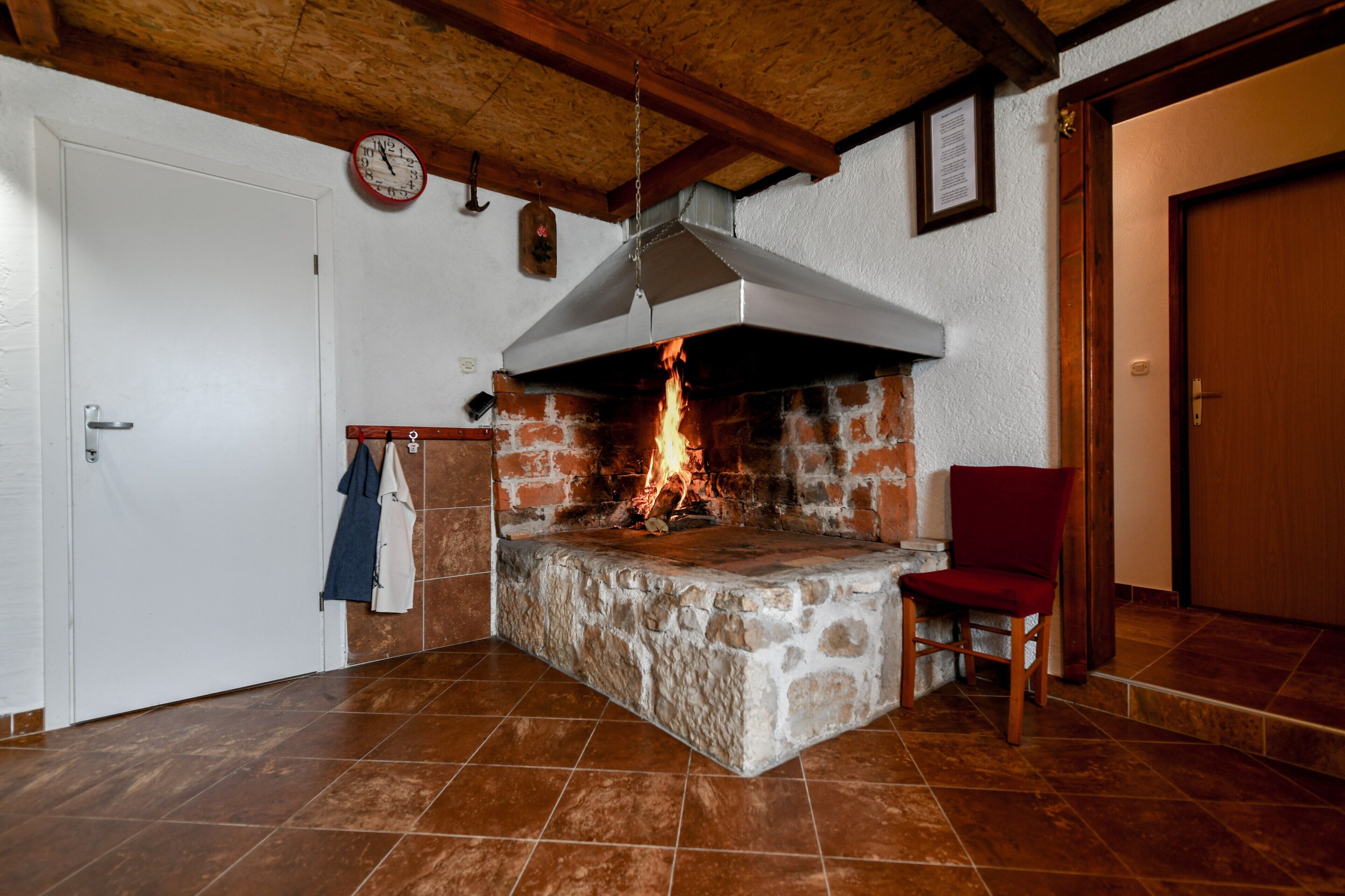 Ein Kamin aus Stein mit Feuer, eine Uhr an der Wand und eine Holzbalkendecke.