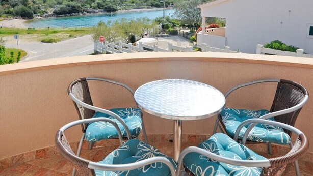 En balkon med et bord og stole, med udsigt over et naturskønt landskab med en flod og bakker.