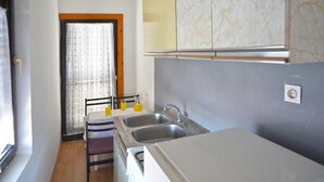 Una cocina compacta con dos fregaderos, un comedor con una silla y una ventana con cortina.