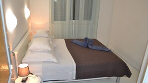 Une chambre d’hôtel avec un lit, une table de chevet avec une lampe et une fenêtre avec des rideaux légers.