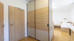 Un dormitorio moderno con suelo de madera, una cama con ropa blanca, una mesita de noche y un armario corredero con acabado en madera clara.