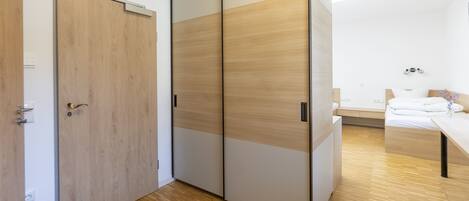 A modern bedroom with a wooden floor, a bed with white bedding, a bedside table, and a sliding wardrobe with a light wood finish.