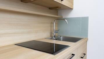 Una cocina moderna con un lavamanos de acero inoxidable, una placa de inducción negra y armarios de madera.